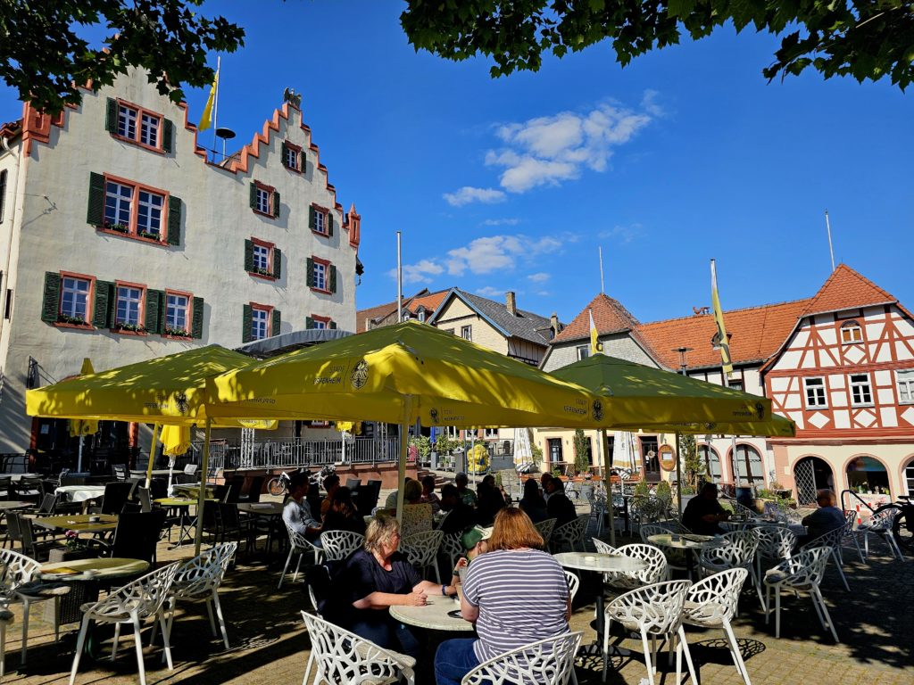 Belebter Marktplatz in Oppenheim mit gelben Sonnenschirmen und Fachwerkfassaden – einladender Treffpunkt für Besucher.