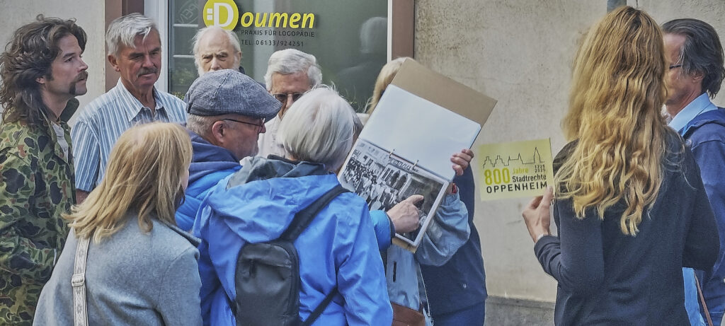 Guest guide Thomas Ehlke (2nd from left) explains the former range of stores at the foot of Mainzer Straße to the audience, while Ulla Eisenhardt (center) holds up the accompanying photos.