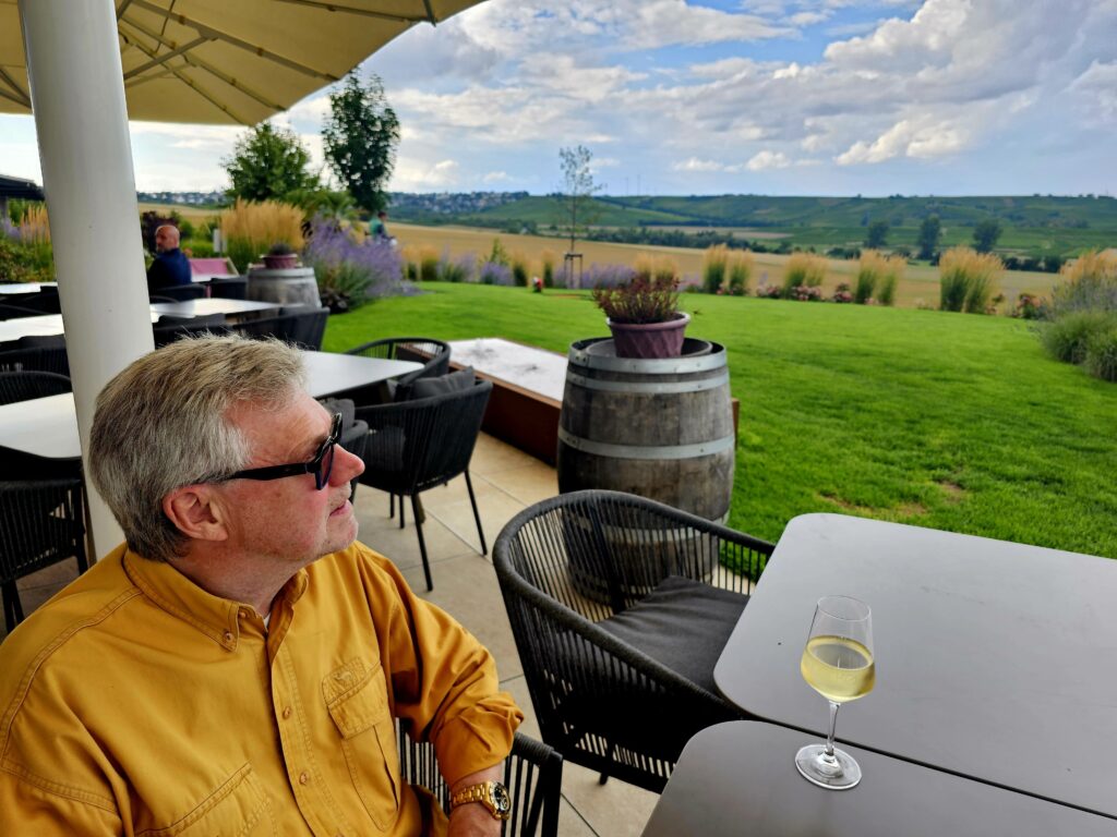 Mann genießt ein Glas Weißwein mit Blick über ein weites Rebenmeer