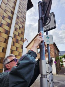 Wegepate entfernt fremde Sticker, die eine Wanderweg-Markierung überkleben.