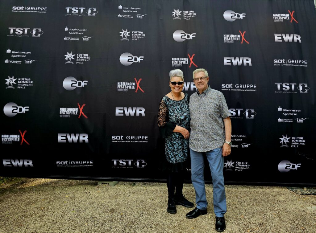 Marina Noble und Rainer vor der Sponsorenwand der Nibelungen-Festspiele